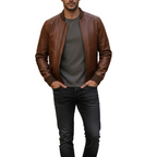 Man wearing a brown leather jacket, gray shirt, and black jeans on a white background with a brand logo.